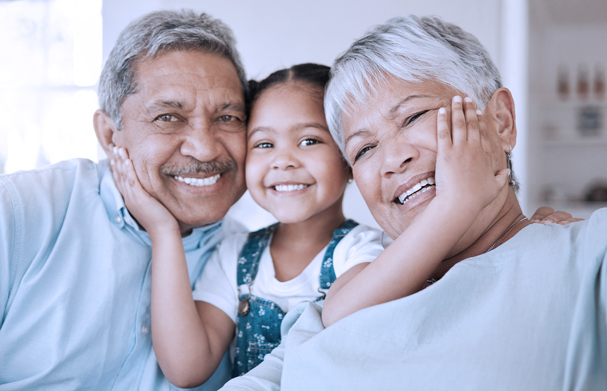 toddler girl smiling and holding the faces of her grandparents