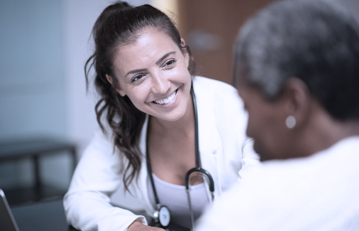 Female nurse practitioner smiles while talking to female patient.