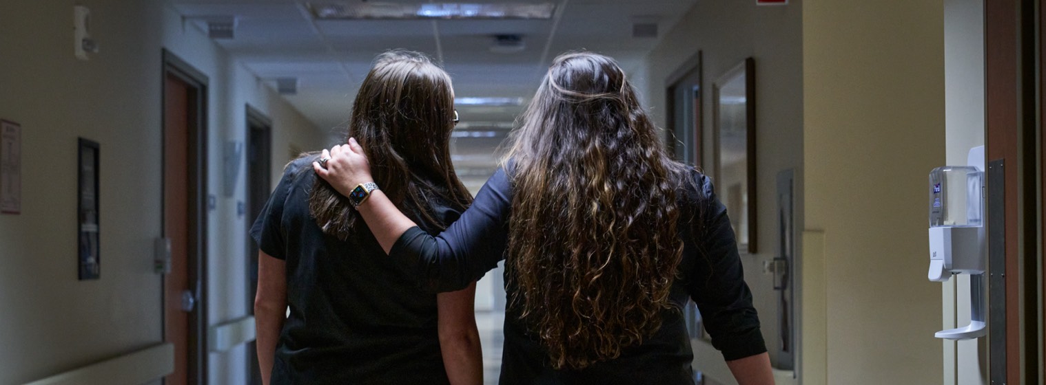 two female nurses walking down a hallway with arms around each other