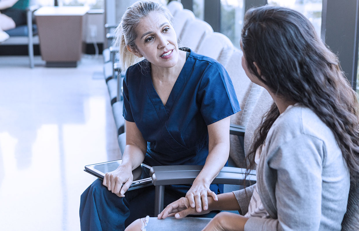 A nurse with a tablet comforts a woman in the waiting room