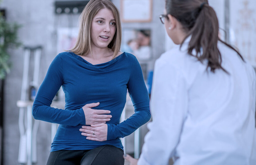 一名妇女抱着她的肚子，医生和她谈论胃肠问题