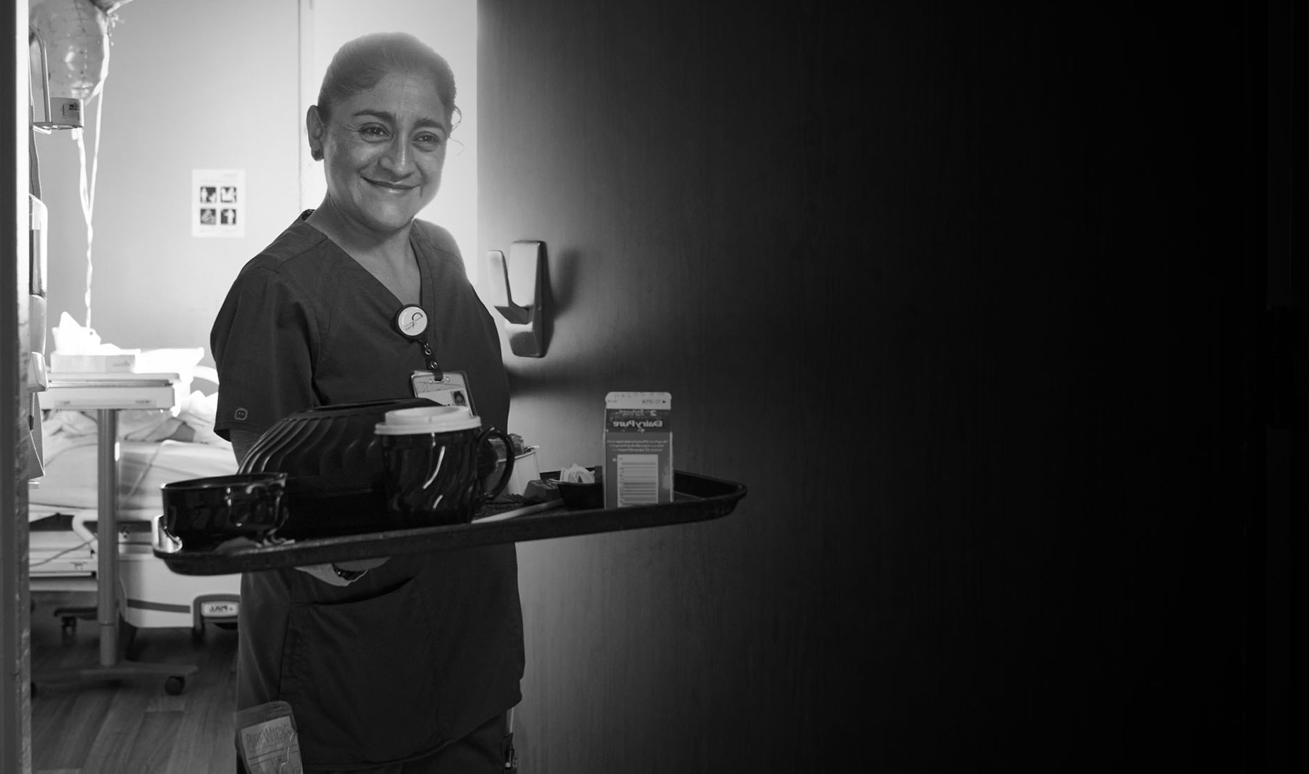 black and white photo of nurse with with tray leaving patient room