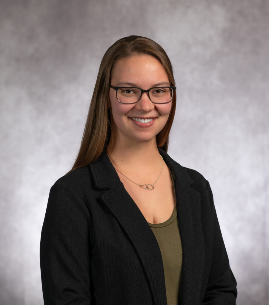 Headshot of Abigail in black suit, wearing glasses.