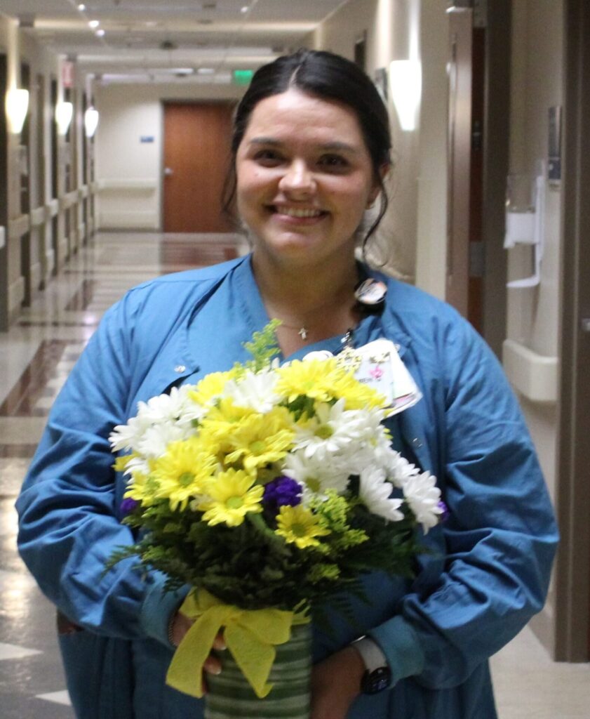 Carmen in scrubs holding daisies.
