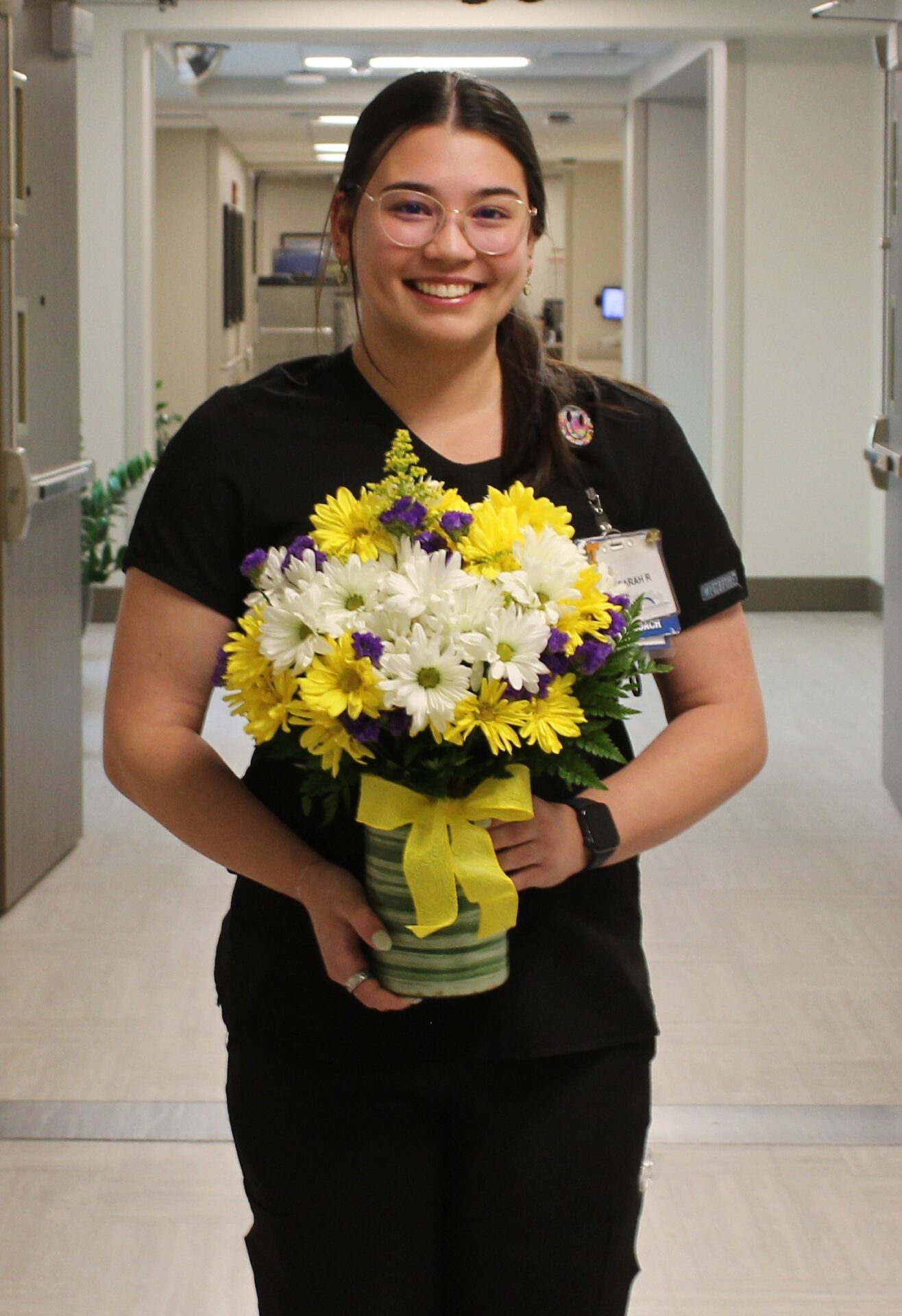 Sarah pictured in black scrubs holding her DAISY arrangement.