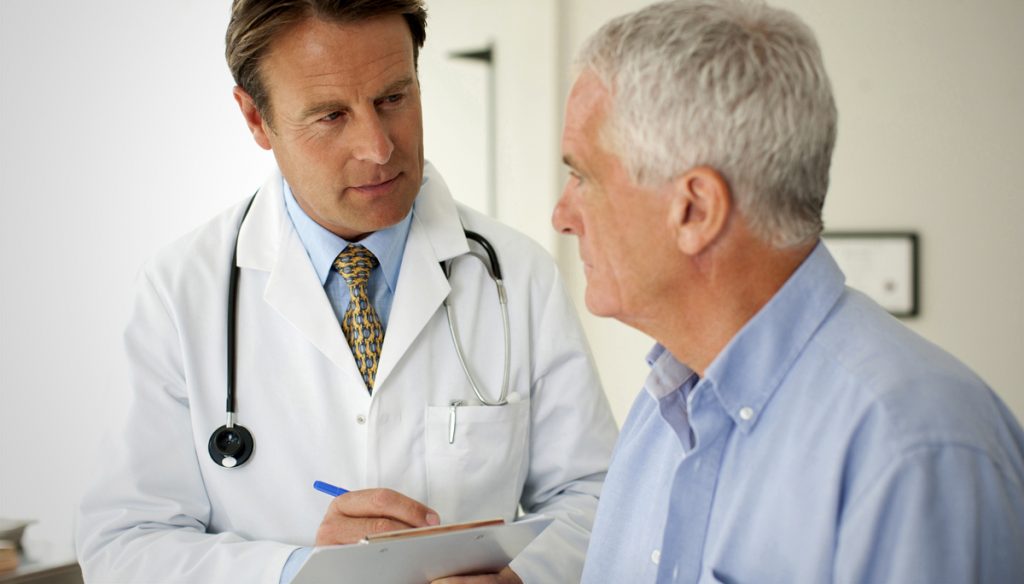 Male doctor speaks to older male patient in a clinic setting