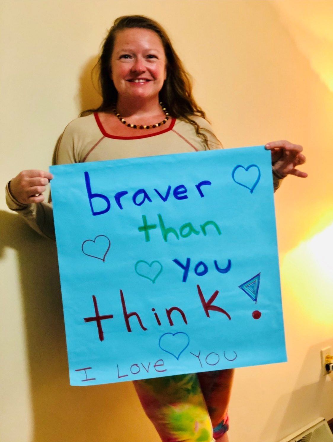 Michelle Watkins holds a sign that says "braver than you think!"
