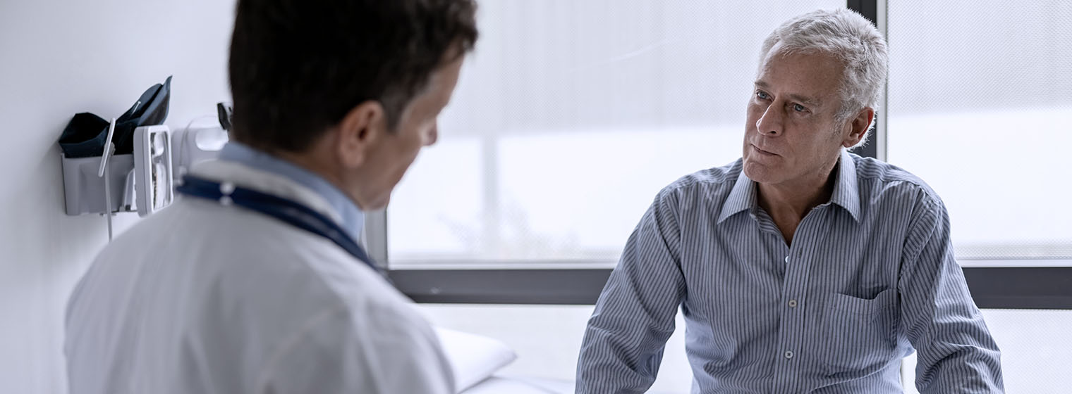male doctor in white coat speaks to an older white-haired man in a doctors office
