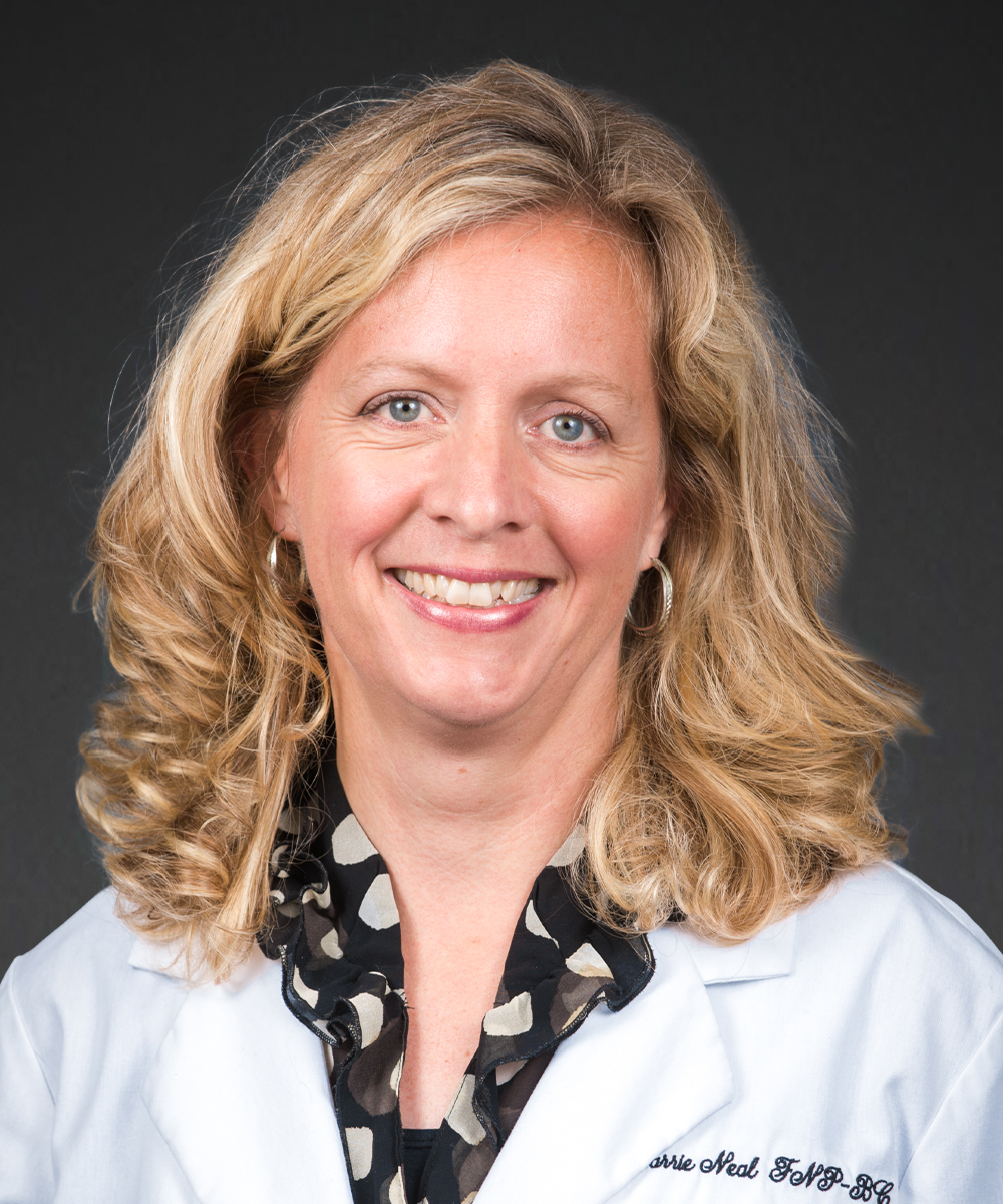 A smiling woman with blond, curly hair wears a white lab coat and a black blouse with a patterned collar, standing against a dark background—a poised professional representing the expertise of MedCare Specialists.