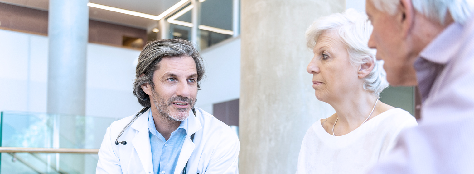 Male physician explains cancer treatment options to senior couple at the hospital.
