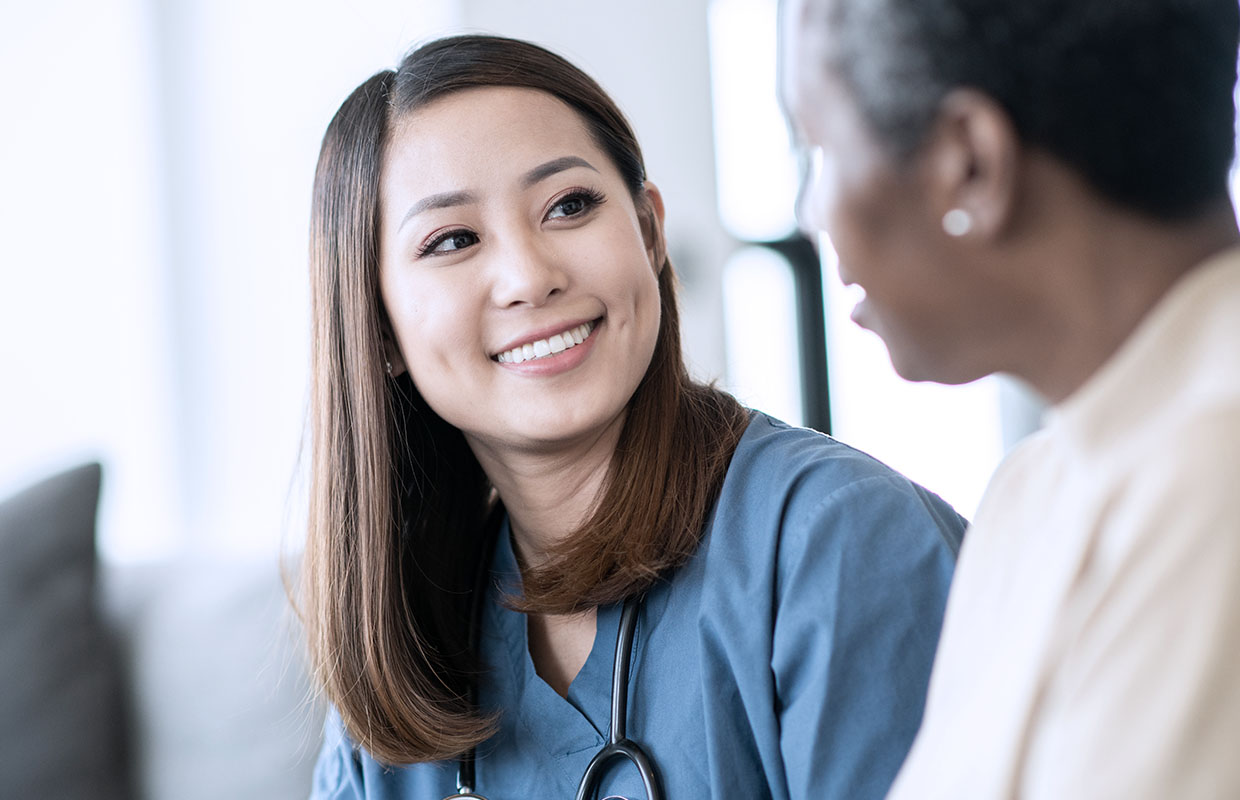 a behavioral health nurse in blue scrubs smiles and talks to an elderly african-american female patient