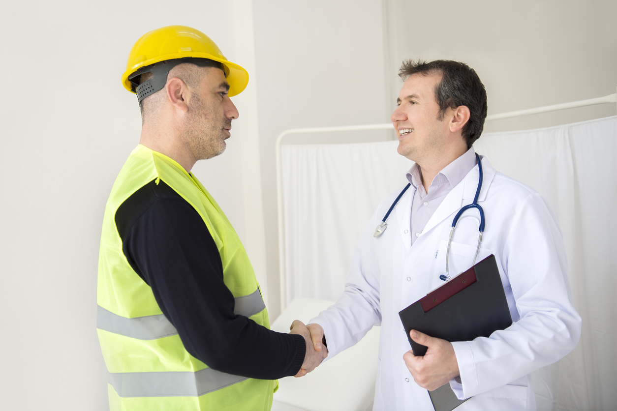 A construction worker in a yellow vest and helmet shakes hands with a smiling doctor in a white coat holding a clipboard, suggesting a workplace health consultation provided by MedCare Specialists.