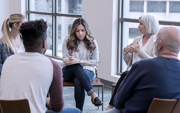 woman leads group therapy session with 4 people sitting in a circle