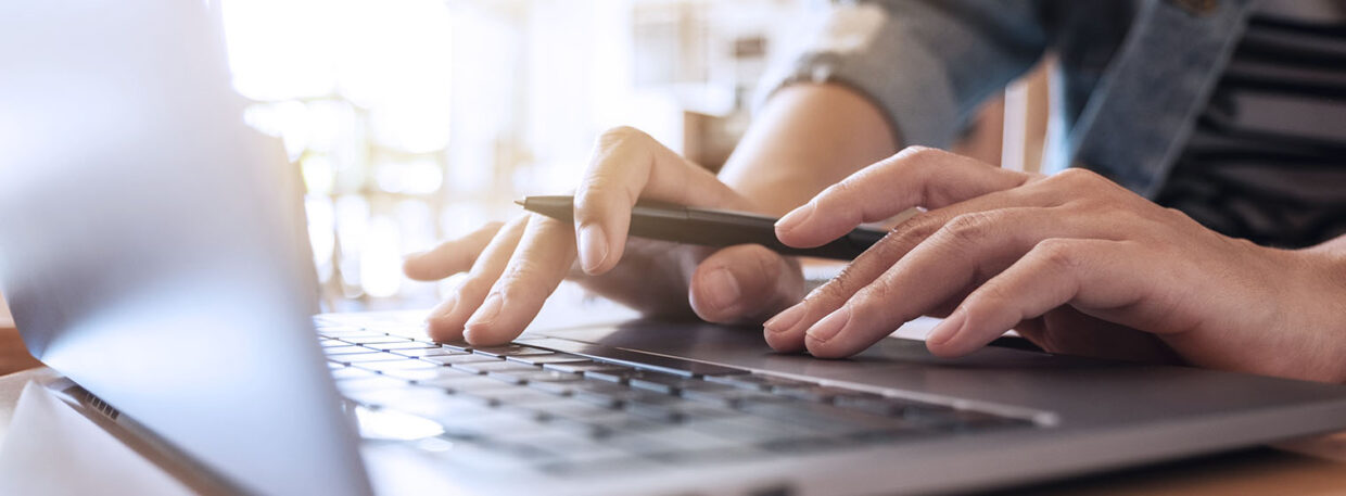 closeup of hands typing on a computer with a pen in the right hand