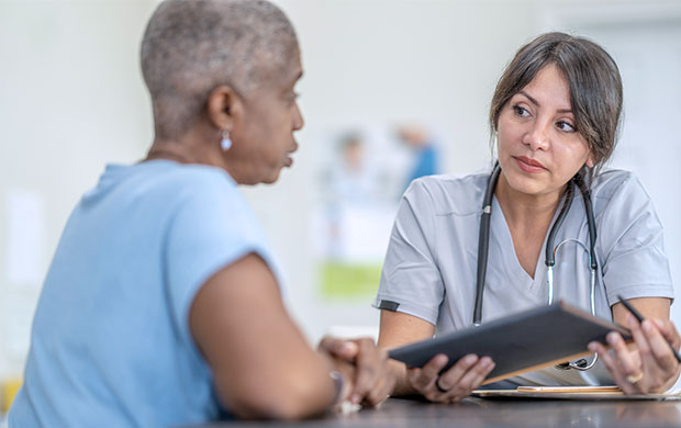 a doctor sits at a table and talks to a patient while holding a tablet