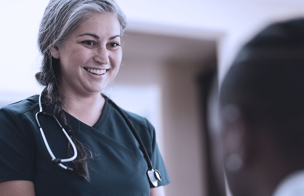 middle age female nurse in green scrubs smiling at a patient