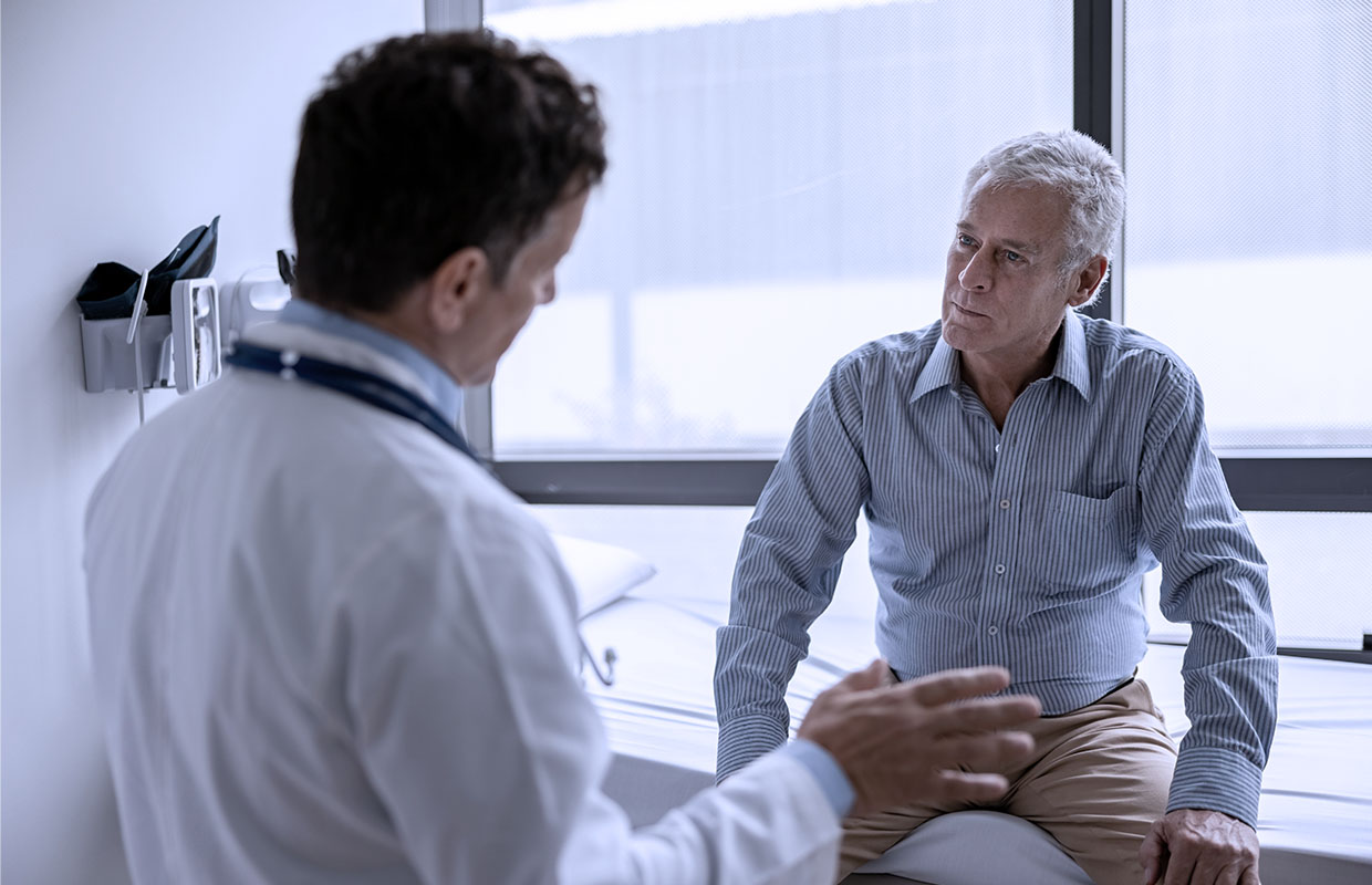 young male doctor talking to elderly male patient sitting on bed