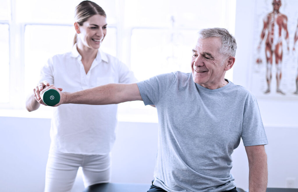 young female physical therapist helping senior male patient lift weight as part of outpatient rehabilitation 
