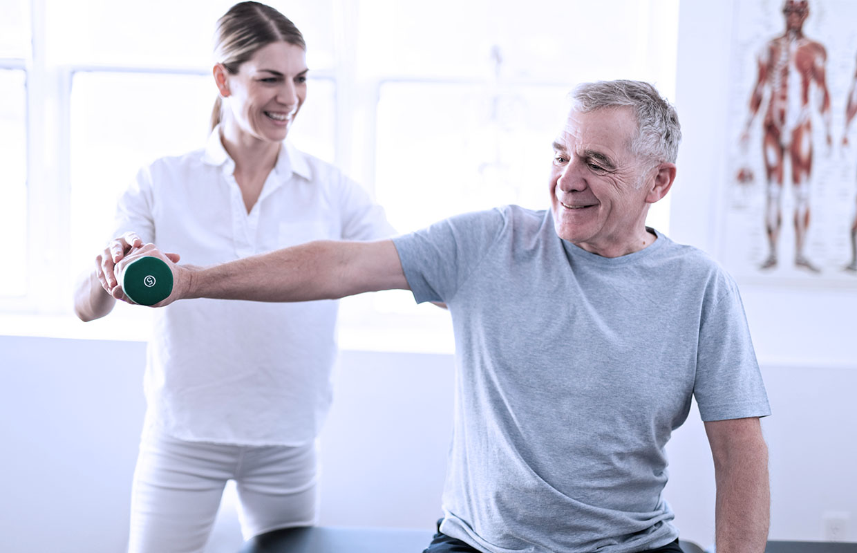 young female physical therapist helping senior male patient lift weight