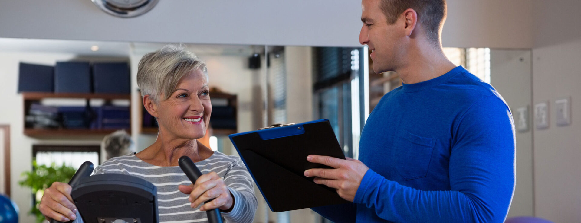 A middle age man smiling at his elder patient for her cardiac rehab.