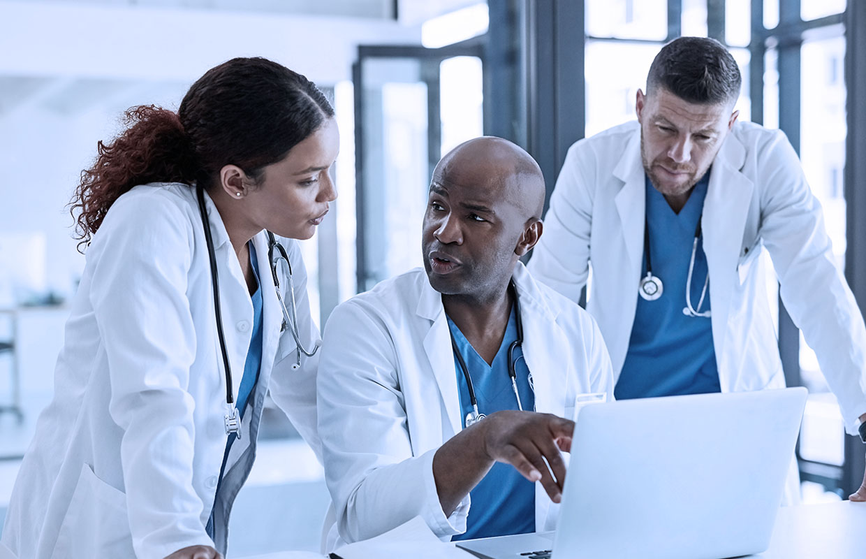 senior male doctors showing two young doctors something on laptop screen