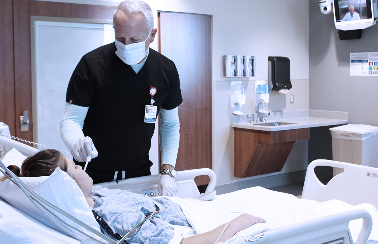 male nurse taking temperature of young female patient with doctor on screen