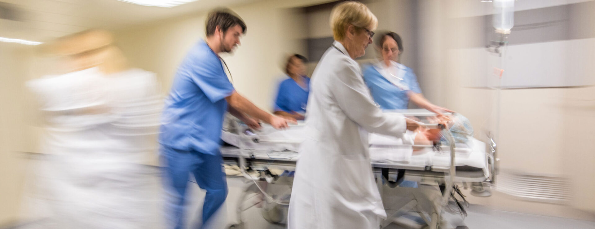 nurses and doctors rushing through hospital hallway with patient bed blurred