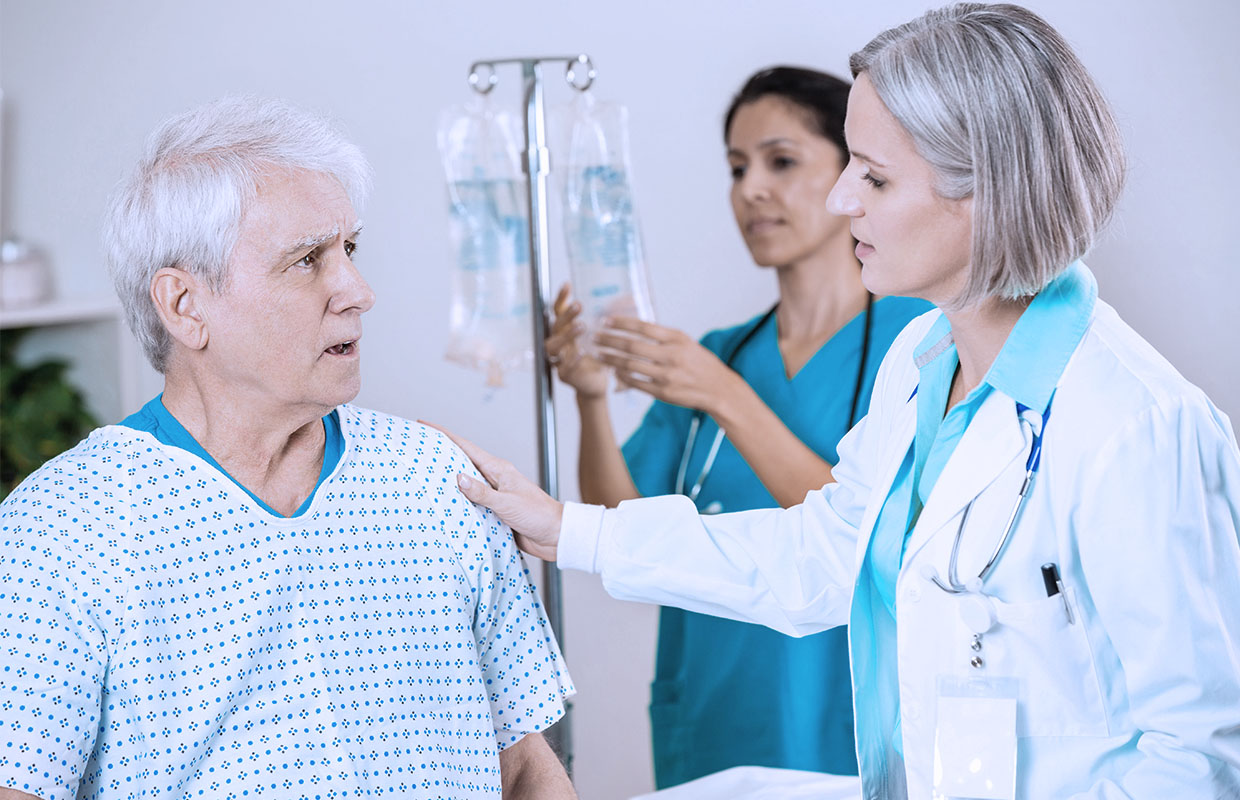 doctor talks to male patient while a nurse prepares an IV bag