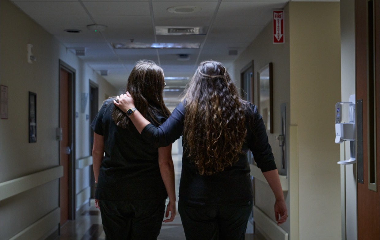 Two female nurses walk down the hospital hallway.