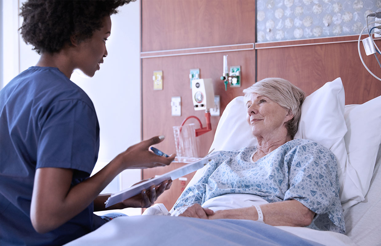 elderly woman in hospital bed talking to young female nurse