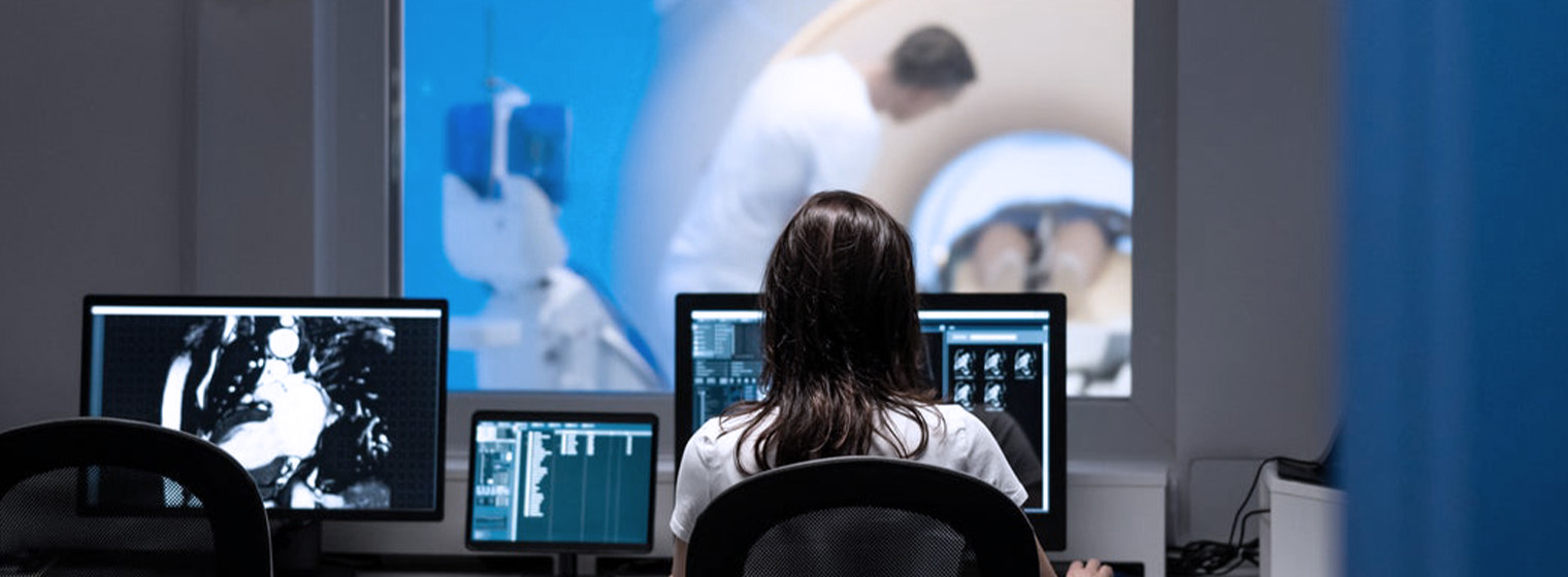 radiologist looking at computer screens while another radiologist preps a patient for a scan