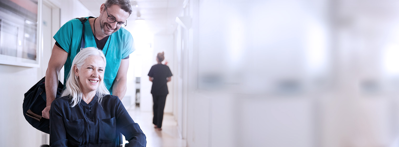 male nurse helps push elderly female patient in wheelchair through the hospital