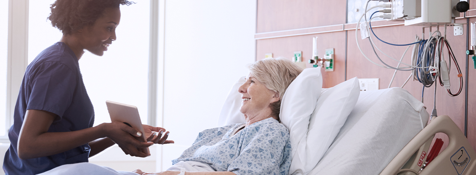 young female nurse showing results to elderly female patient laying in hospital bed