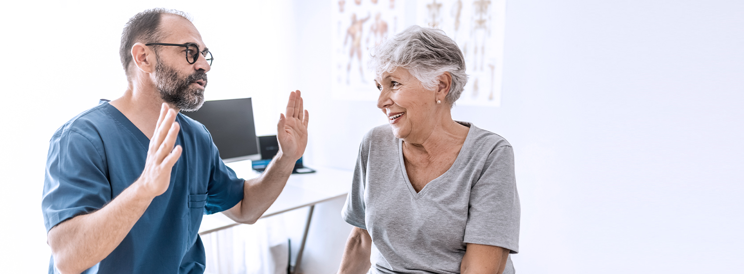 male doctor holding his hands shoulder width apart while talking to elderly female patient