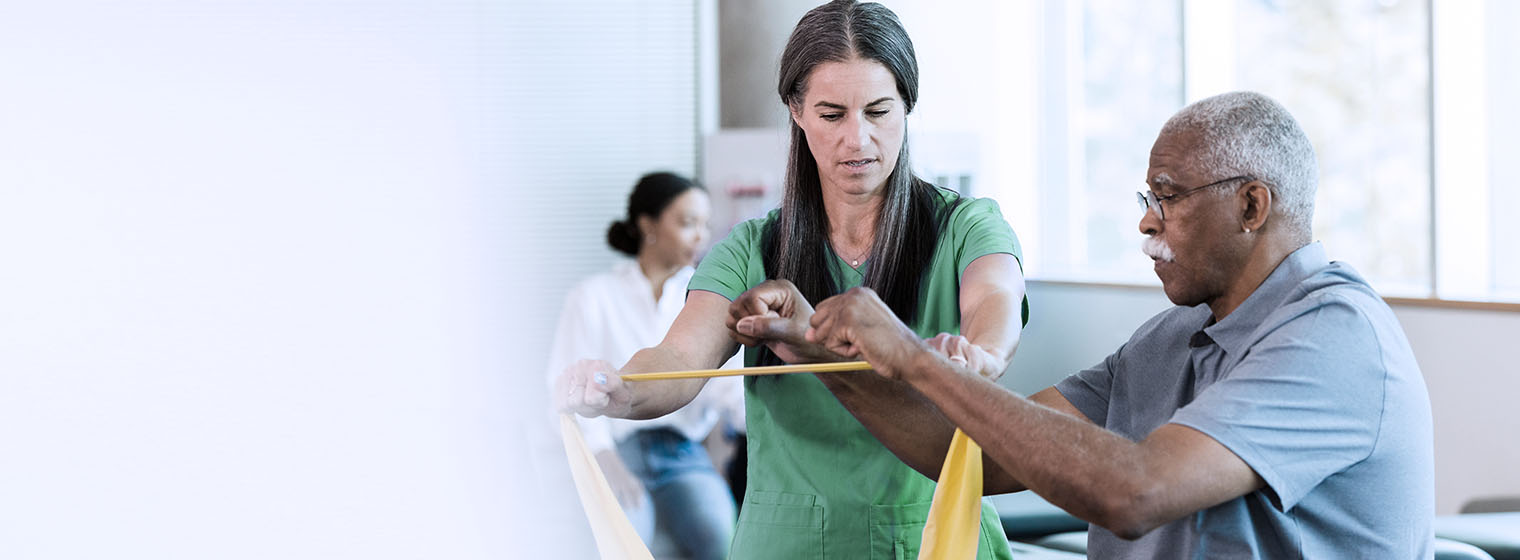 young female therapist in green scrubs assists an elderly male patient with his therapy