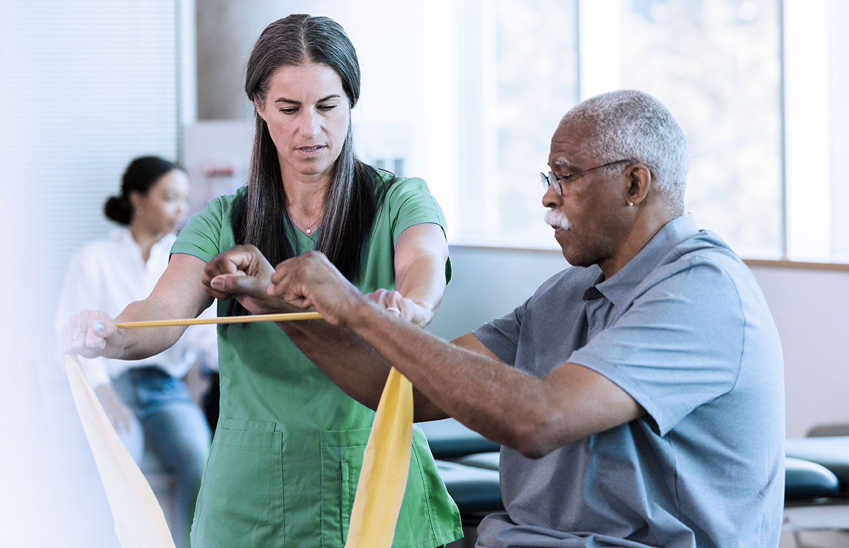 young female physical therapist in green scrubs helping elderly male patient with his therapy