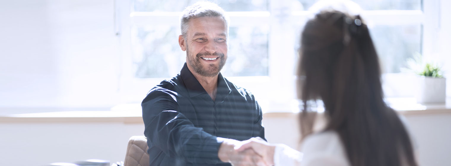 young male shaking hands with a female in front of a window