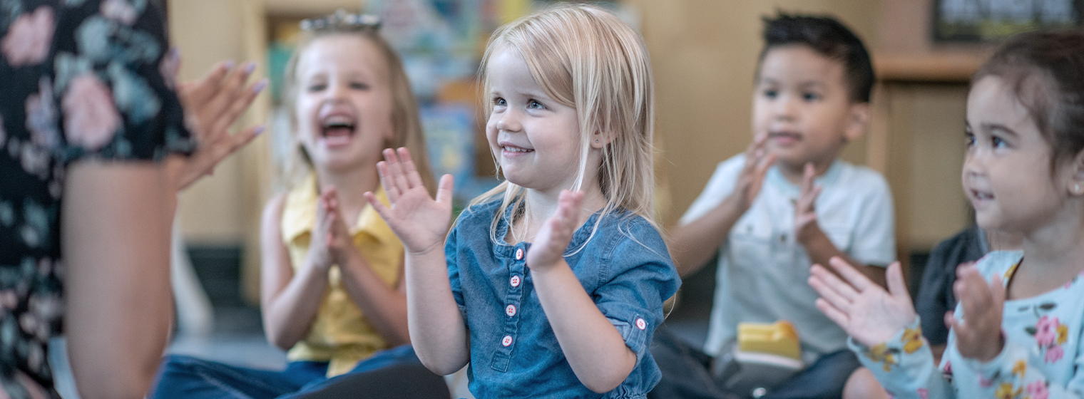 Group of preschool children laugh as they play a game in their classroom.