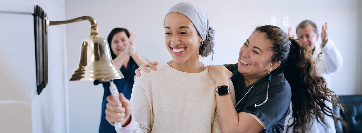 female cancer patient ringing the bell after finishing her cancer treatments with people clapping