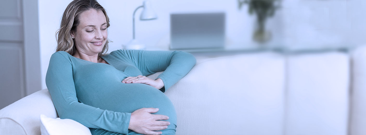 expectant mother smiling and holding her stomach while on the couch