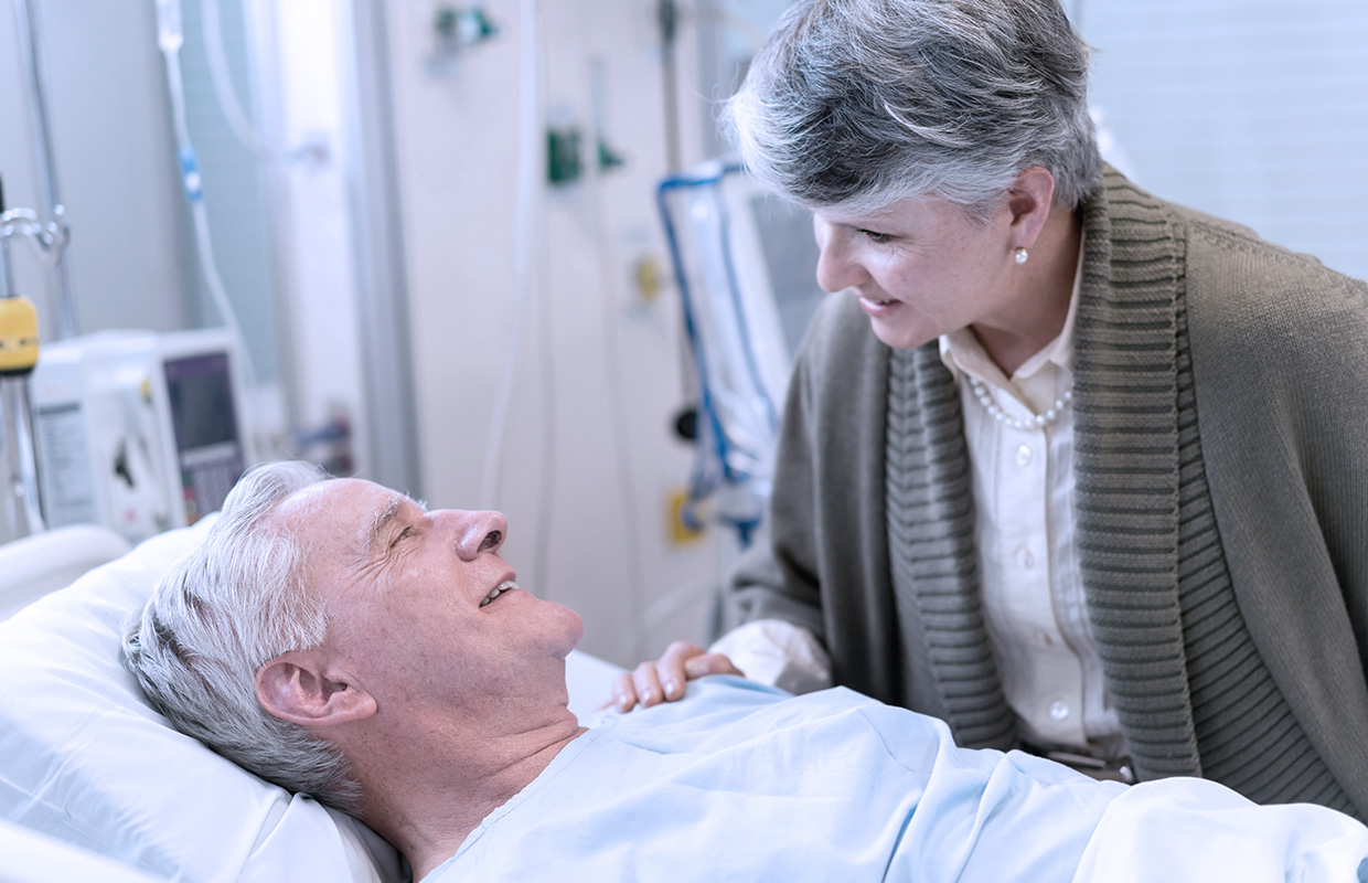 elderly female comforts husband in hospital bed