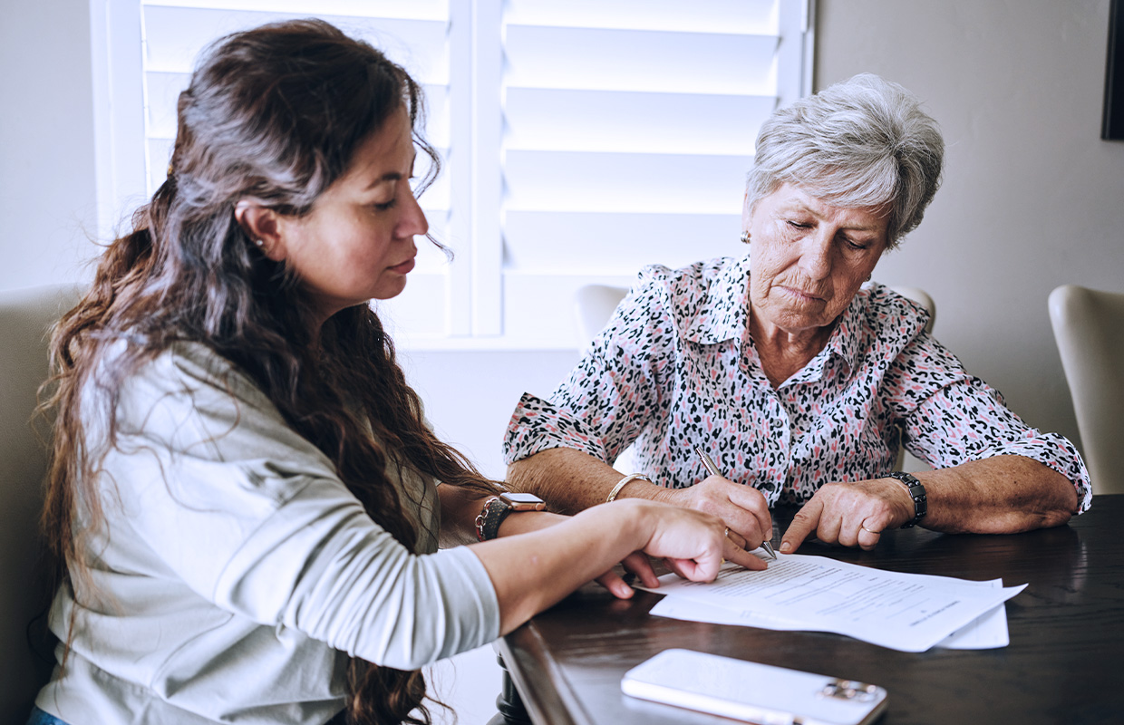 young female showing an elderly female where to sign a piece of paper