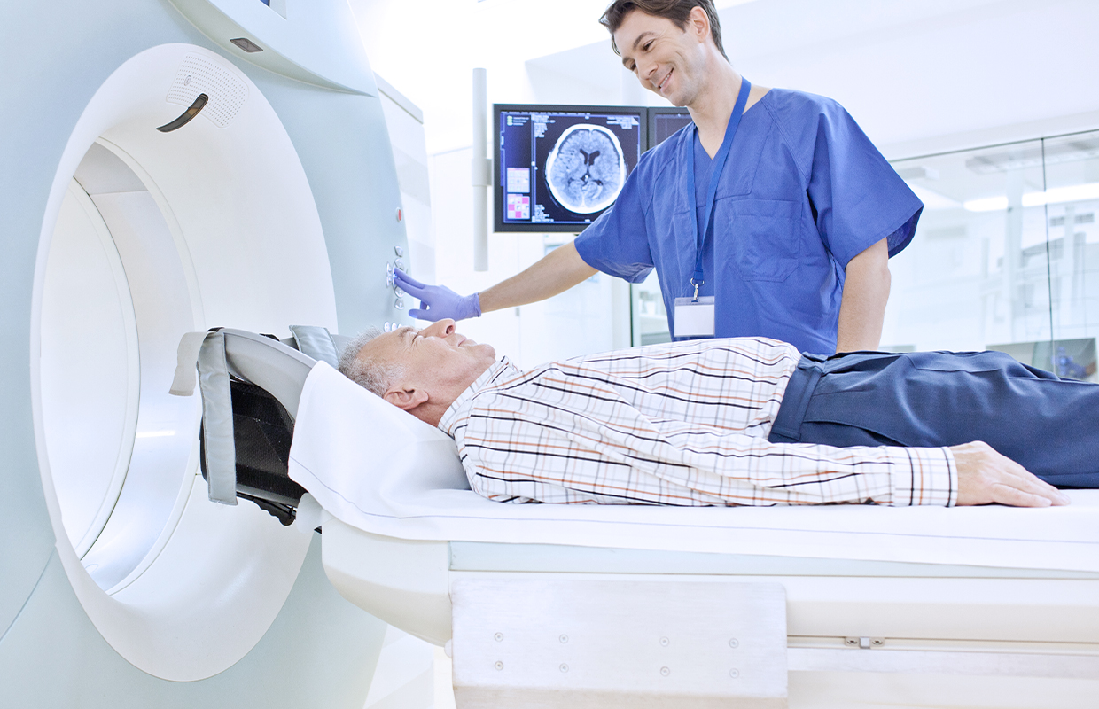 young male nurse in scrubs smiling down at elderly male patient before he enters an imaging machine