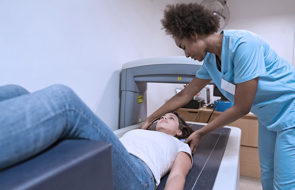 female patient lying down to get bone density testing and nurse in blue scrubs helping