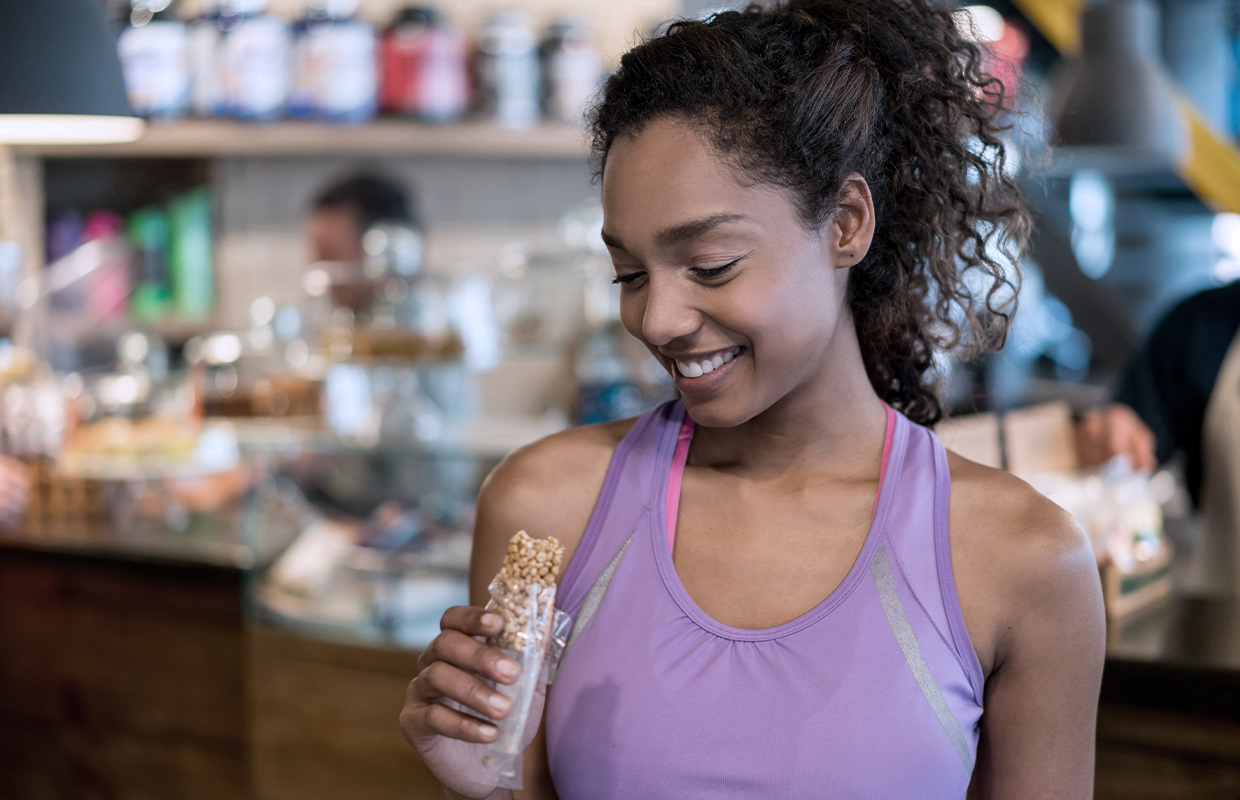 young woman in purple tank eating a granola bar