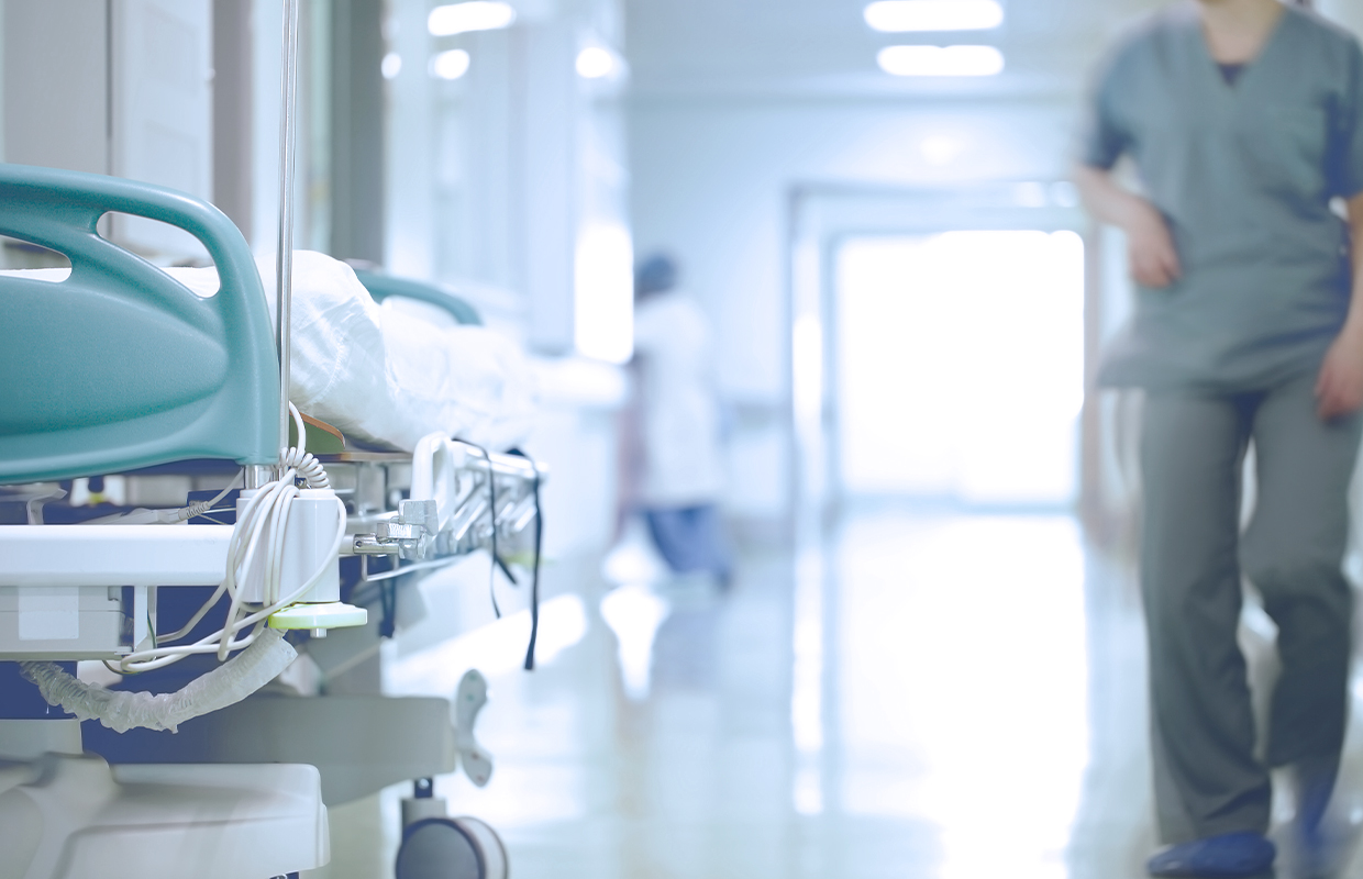 nurse in scrubs walking down hallway next to hospital bed