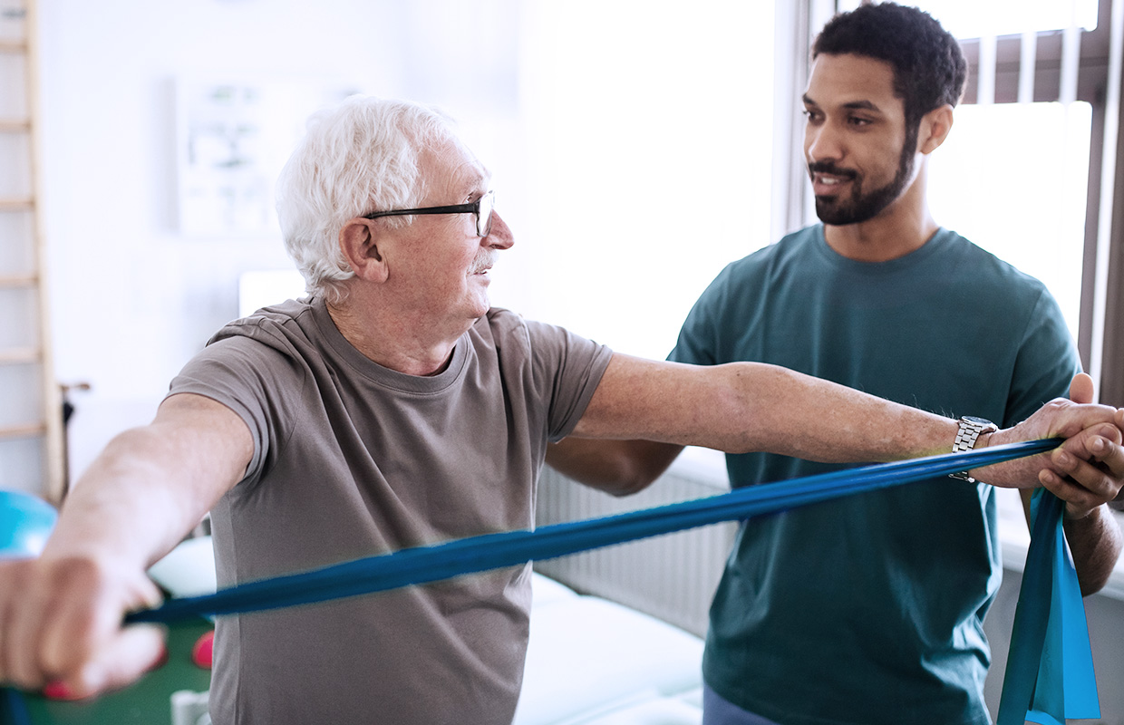 elderly male patient stretching resistance band while young male physical therapist assists