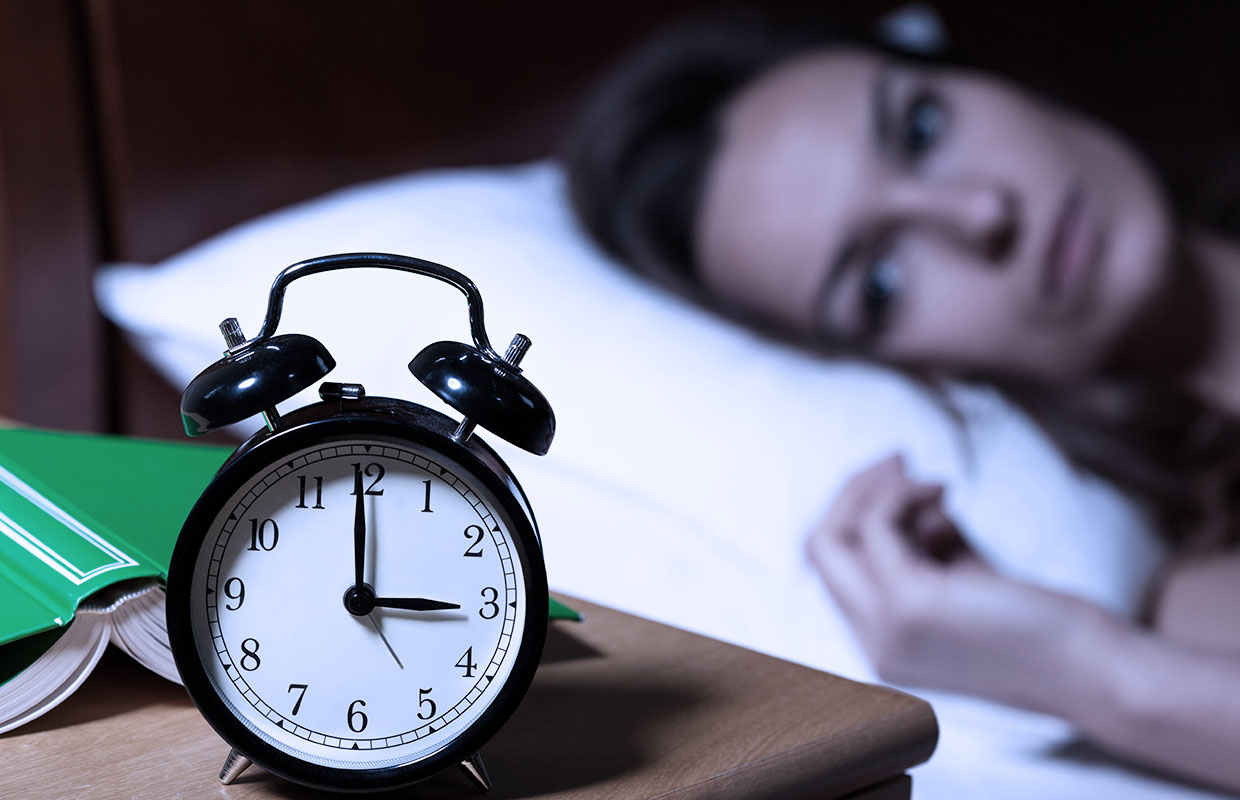 middle-aged female staring at clock in bed