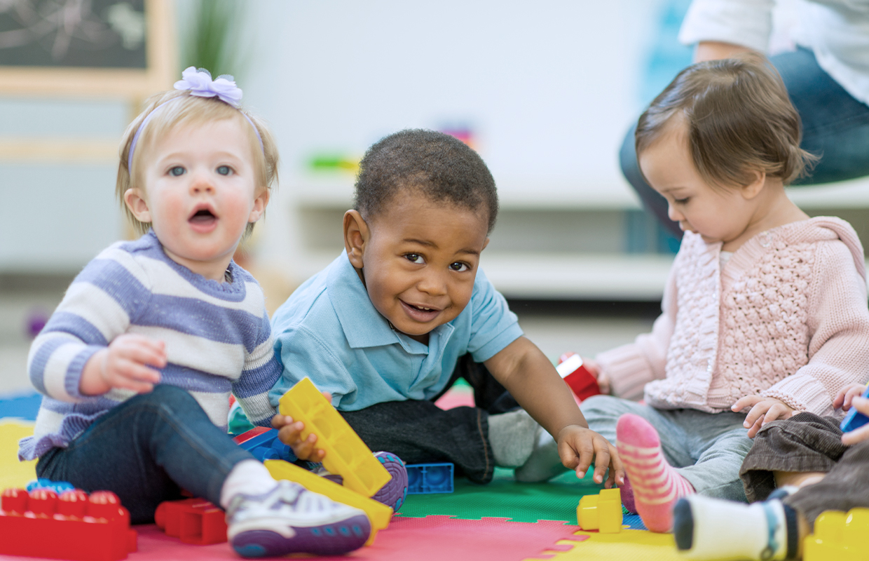 Three toddlers in preschool play with Legos while sitting on the carpet.