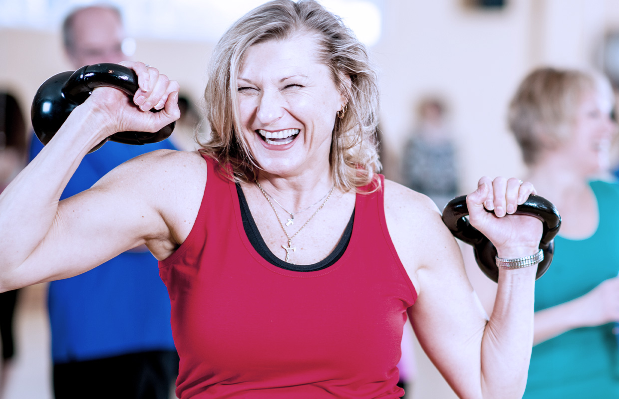 Woman smiling in aerobics class lifting weights.